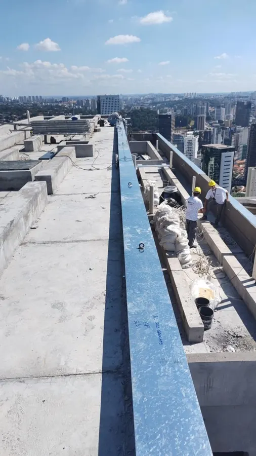 Equipe de capacete instalando rufo pingadeira galvanizado no muro de um prédio alto